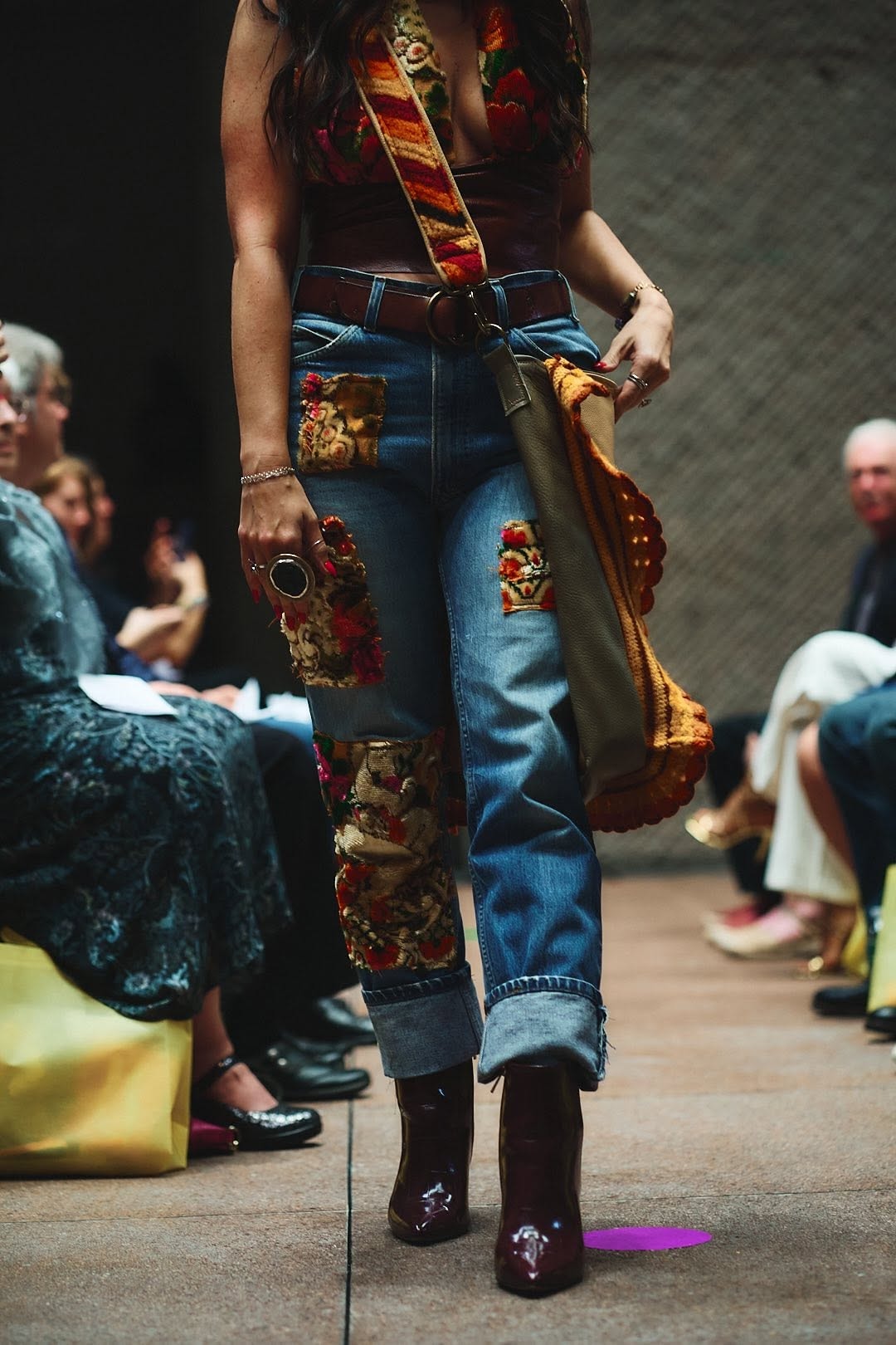 Runway model in tapestry-patched denim jeans and crochet bag